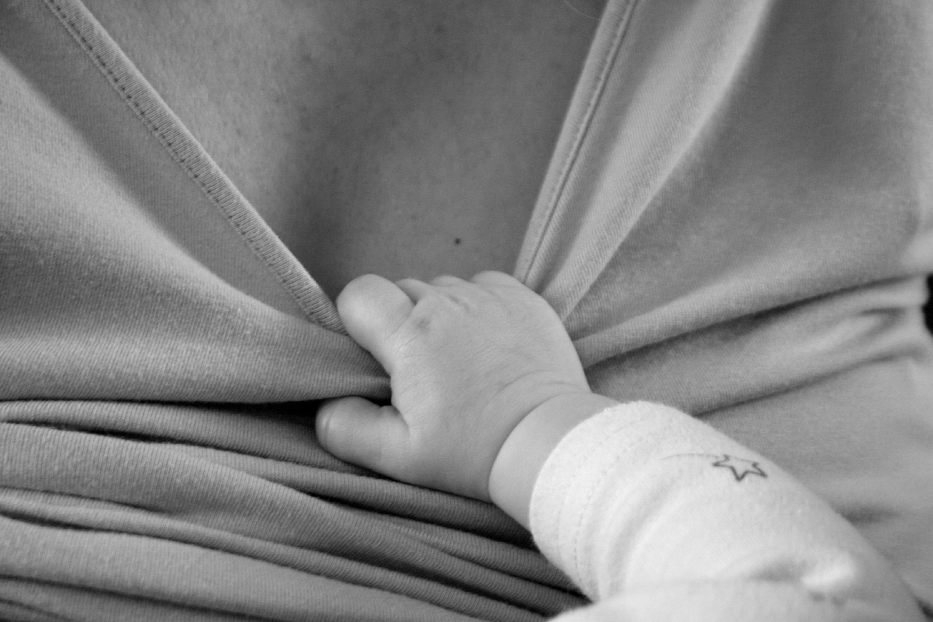 A baby's hand pulling at a mother's top