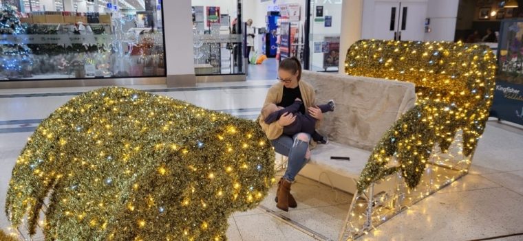 Jessica breastfeeding her 15 month old child, sitting in a sleigh while doing their Christmas shopping. 