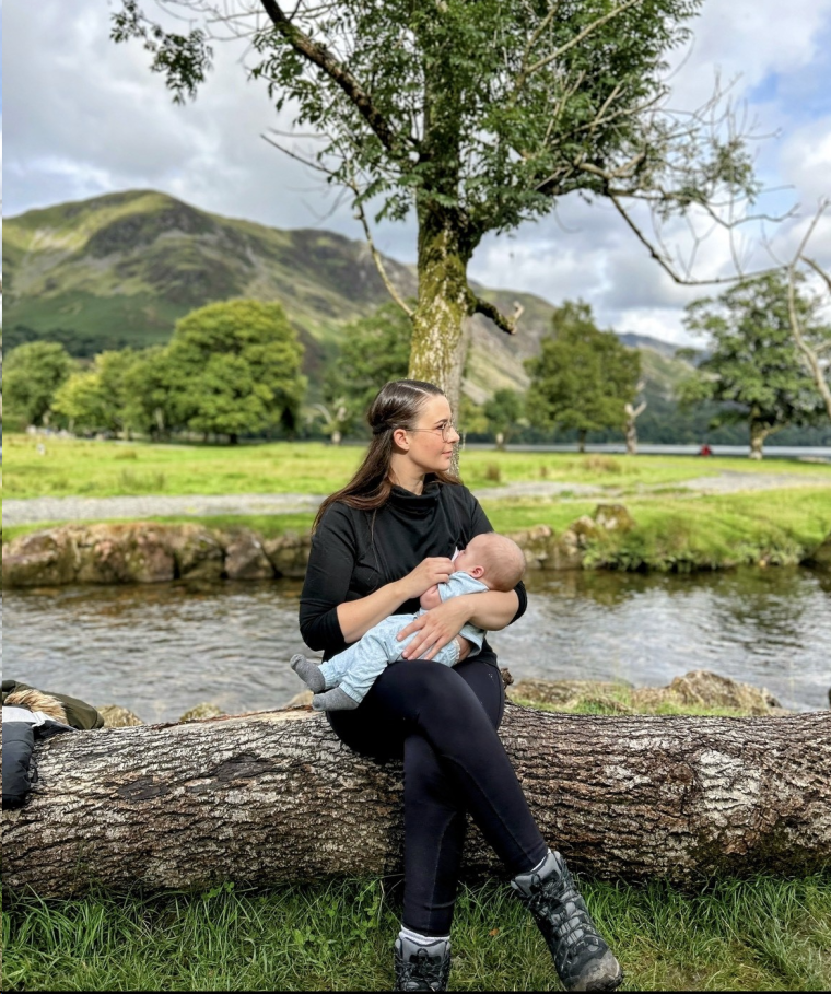 Natalie sitting on a log breastfeeding in the Lake District. 